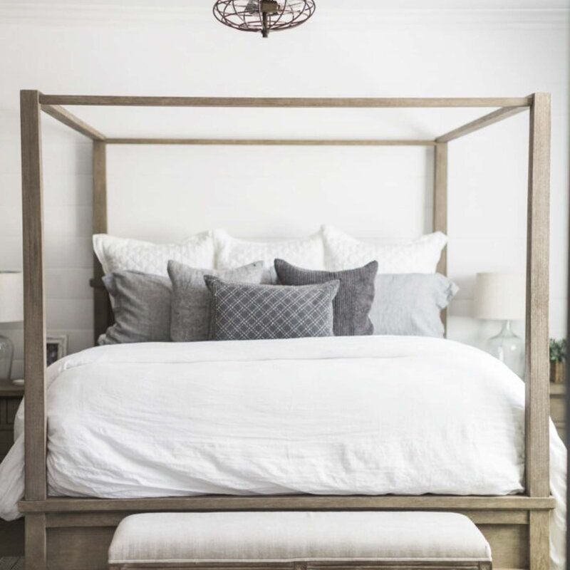 一间白色的卧室，一张木制顶篷床和一台工业风扇