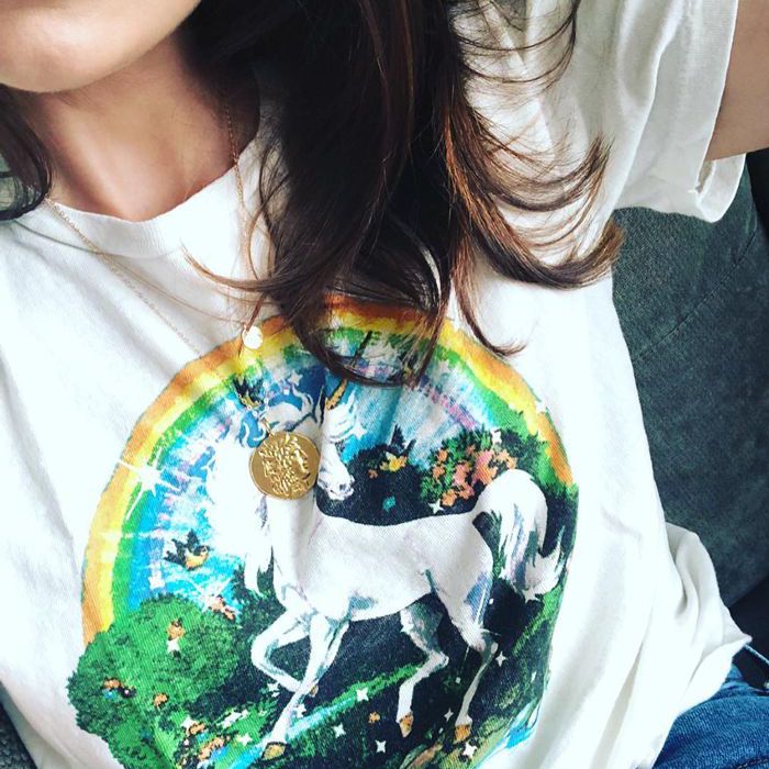一个棕色头发的女孩穿着一件印有独角兽和彩虹图案的白色t恤。