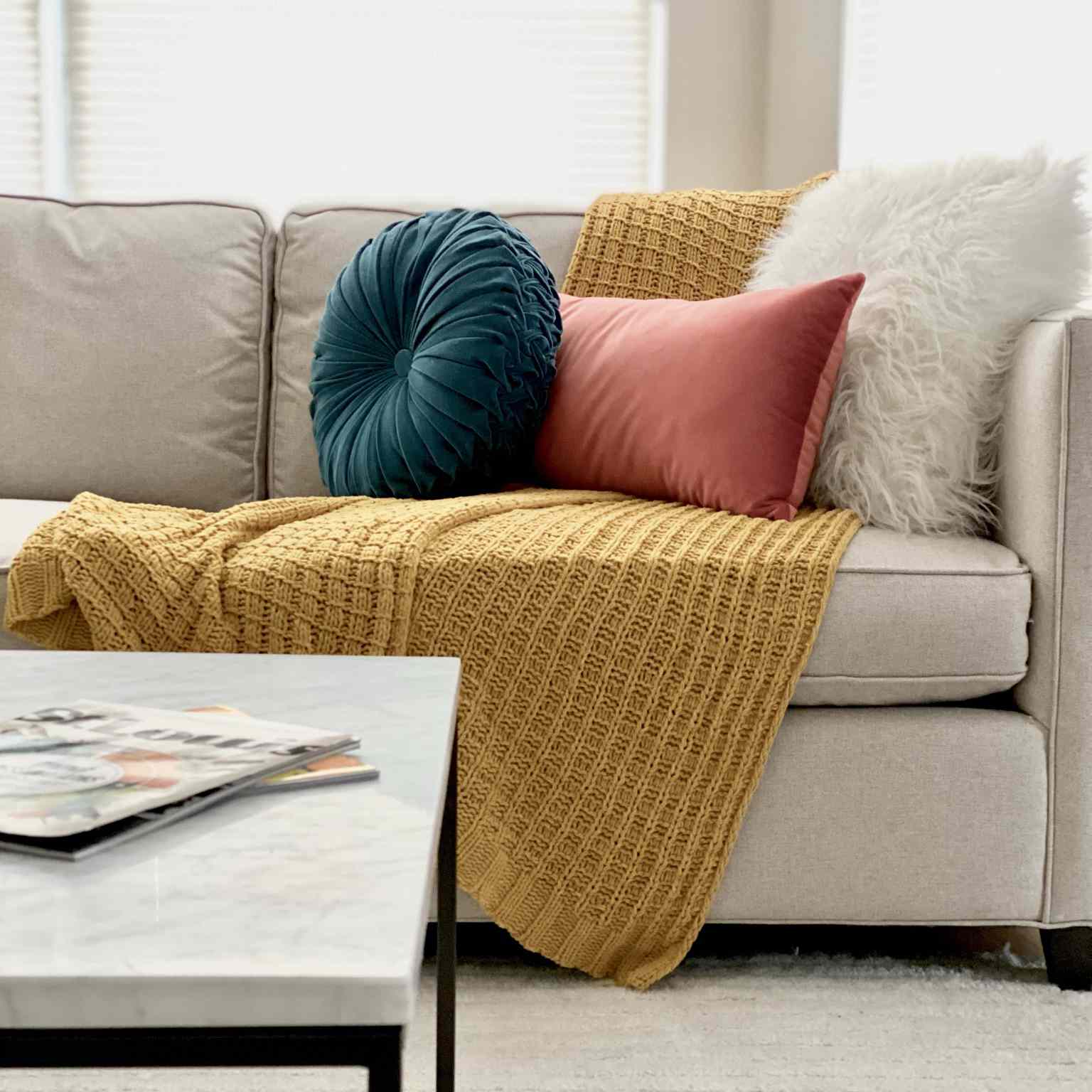 沙发配芥末扔毯子和天鹅绒枕头。