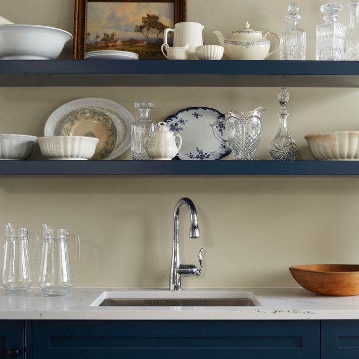 深蓝色的开放式货架展示古董盘子，水晶酒瓶，和一幅画