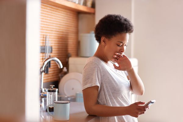 打呵欠在她的厨房的困妇女在一杯咖啡旁边。”class=