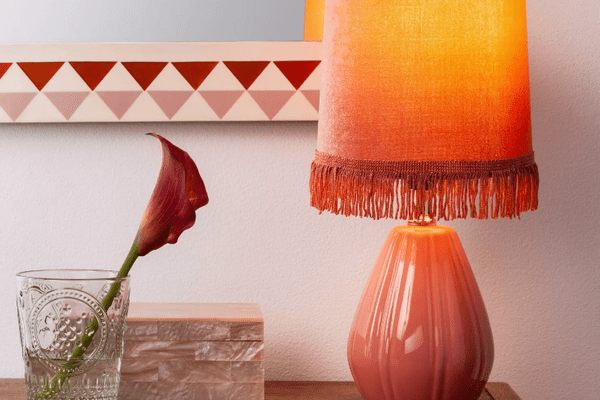 在一个控制台的一盏桃红色桌灯与在坐在装饰箱子前面的一个玻璃花瓶的一个桃红色兰花。