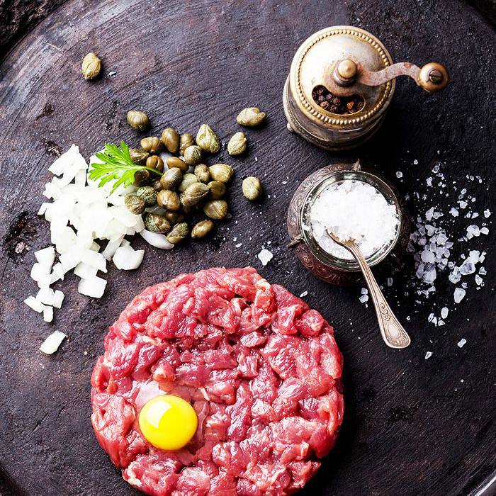 鞑靼牛排放在一个木盘子里，上面放着盐和胡椒