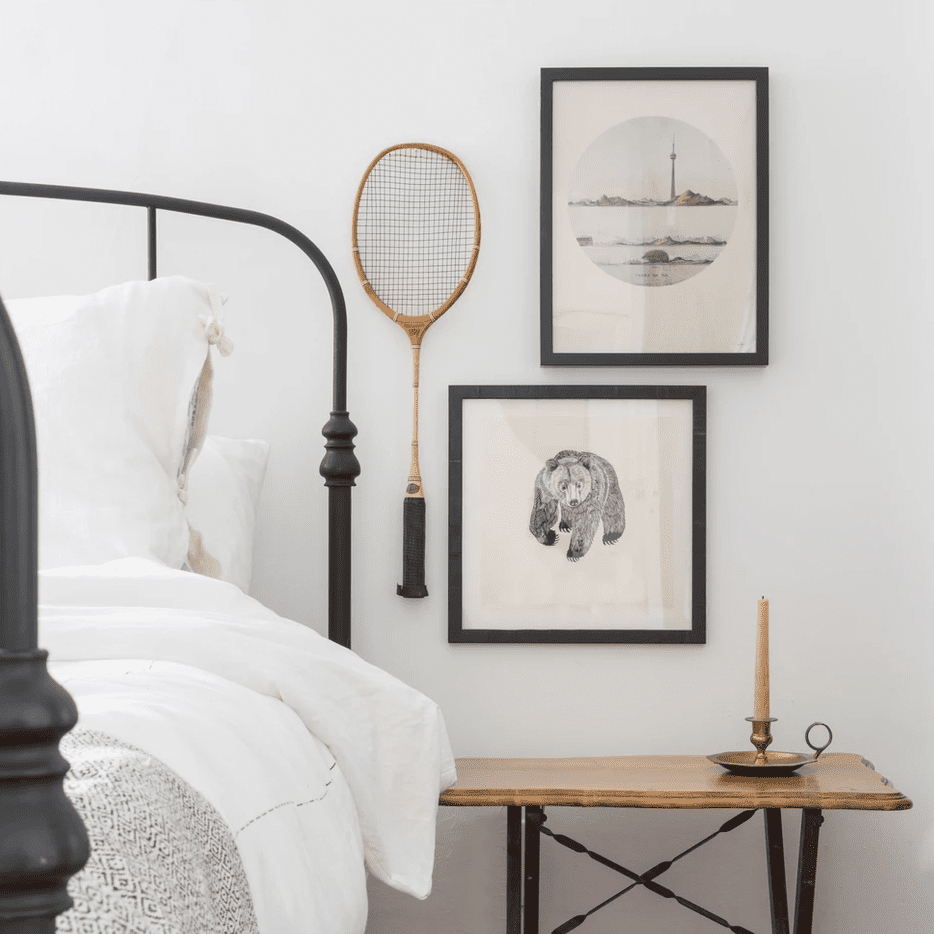 一个小卧室画廊的墙，由两幅版画和一个老式羽毛球拍组成