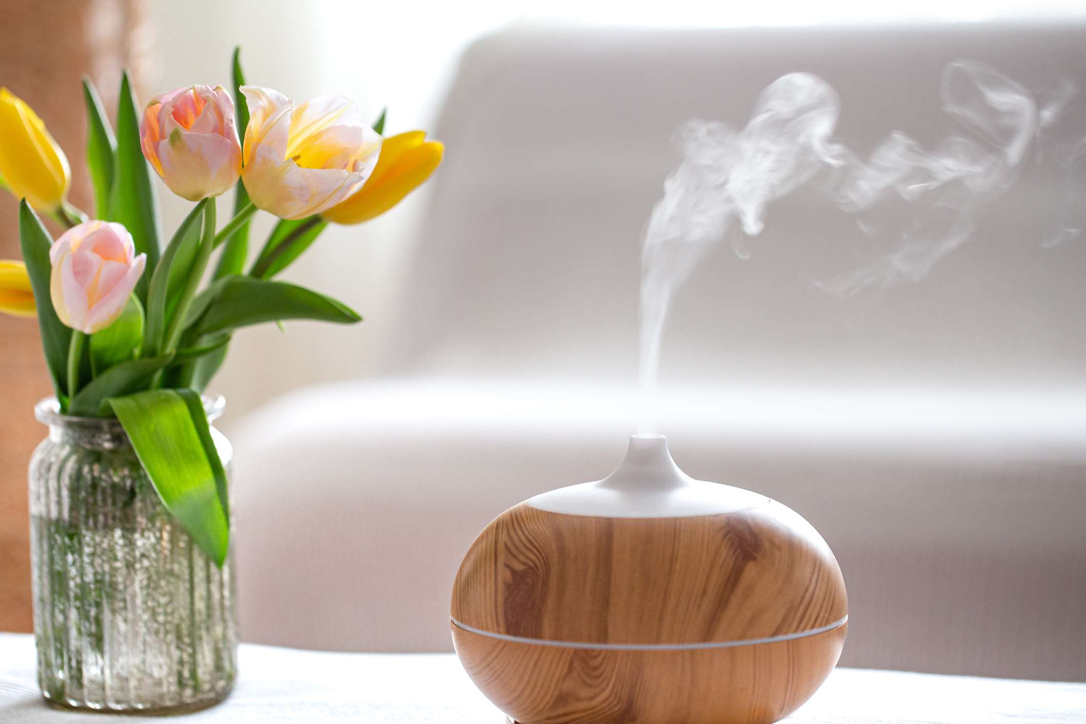 An electric diffuser on a table next to a vase filled with fresh flowers.”class=