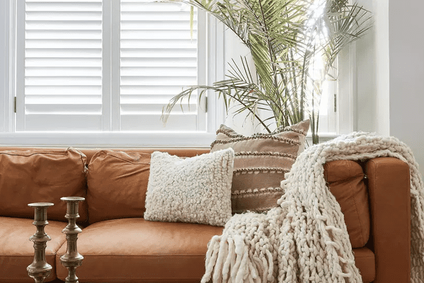 一间配有焦糖棕色皮沙发、米色枕头和米色毯子的客厅