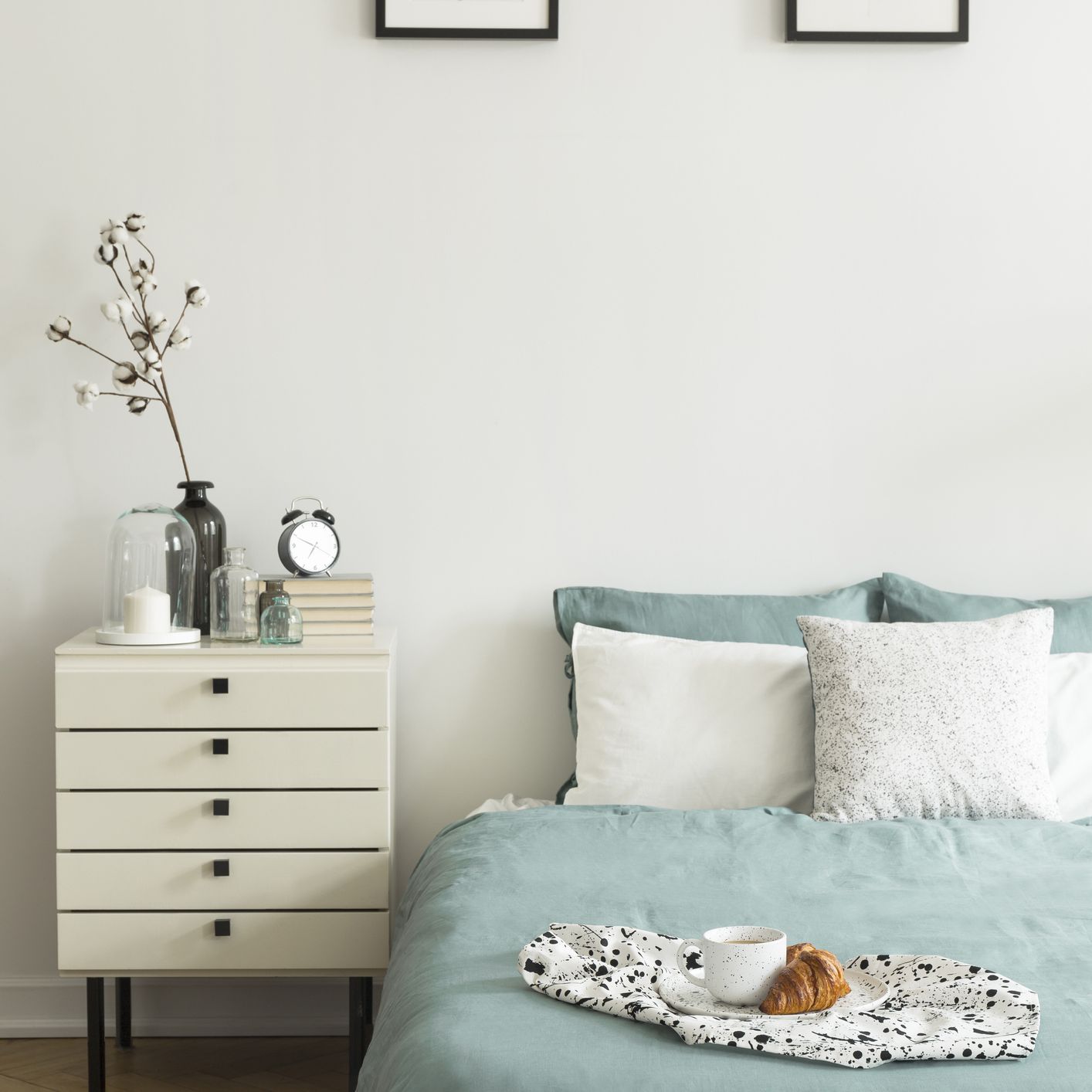 真正的照片白色的卧室内部与早餐放在床上的枕头和柔和的绿色床单，两个简单的海报和装饰床头柜