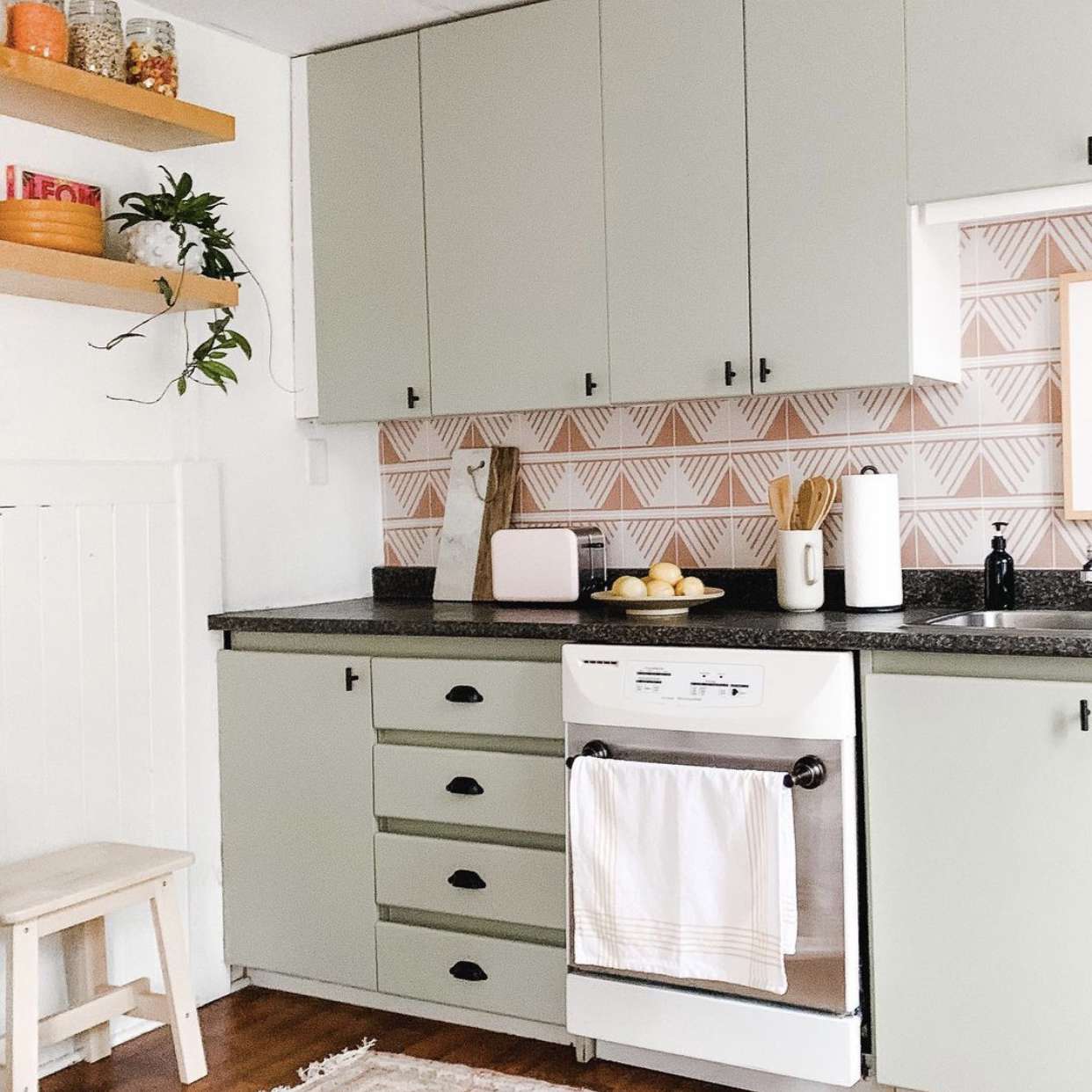 鼠尾草绿色厨房橱柜与粉红色后挡板。