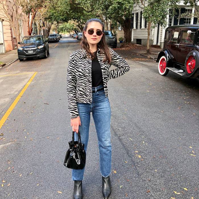一个棕色头发的女孩穿着高腰牛仔裤，斑马纹夹克，太阳镜和黑色皮靴