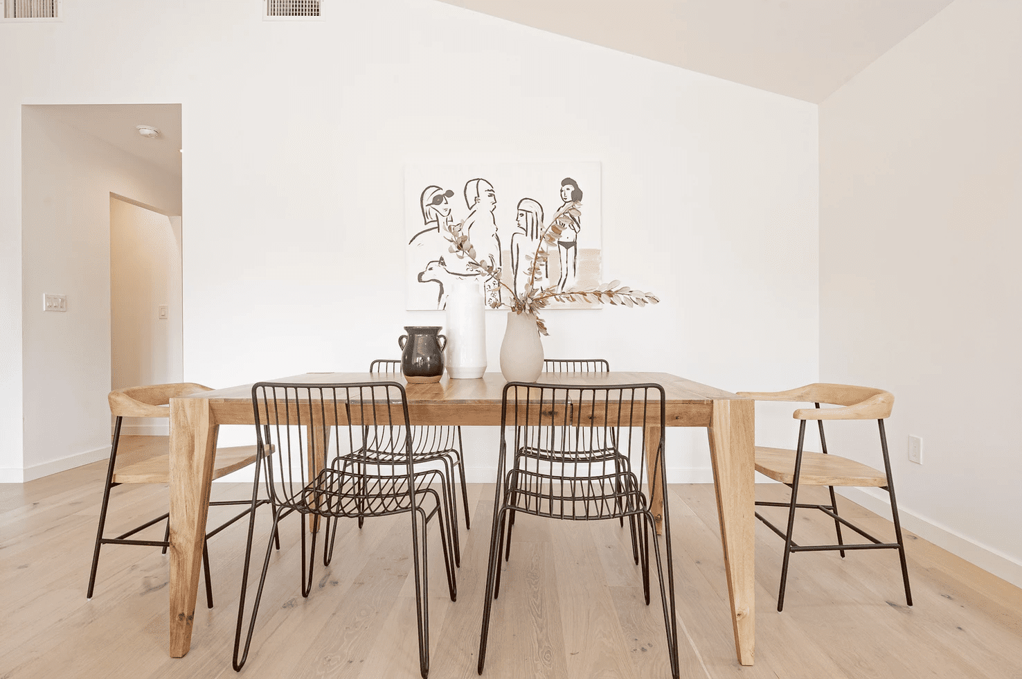 一张木制餐桌，上面装饰着一只黑色花瓶、一只白色花瓶和一只米色花瓶