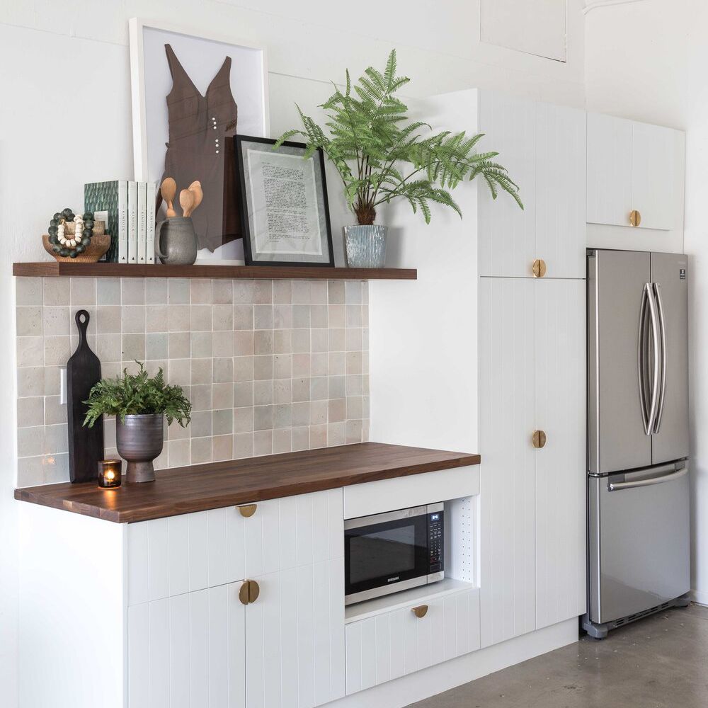 一个小型的白色厨房，带黑色的木制架子和米色的背板