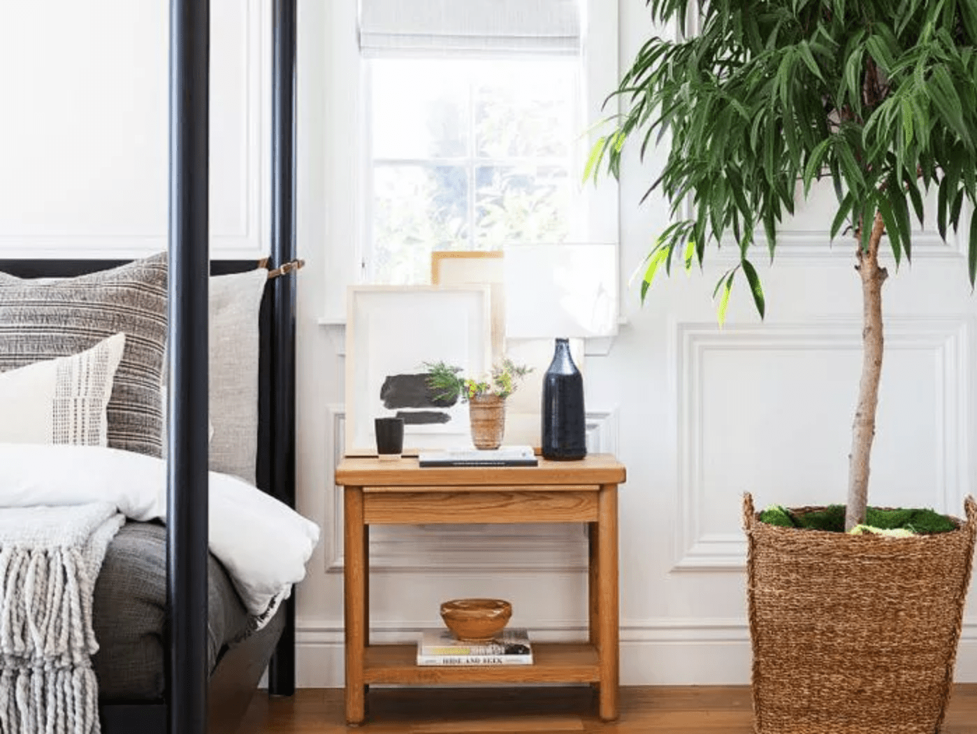 四柱床定位在左窗口，一个木制床头柜放置下方，并在它旁边，盆栽树“class=