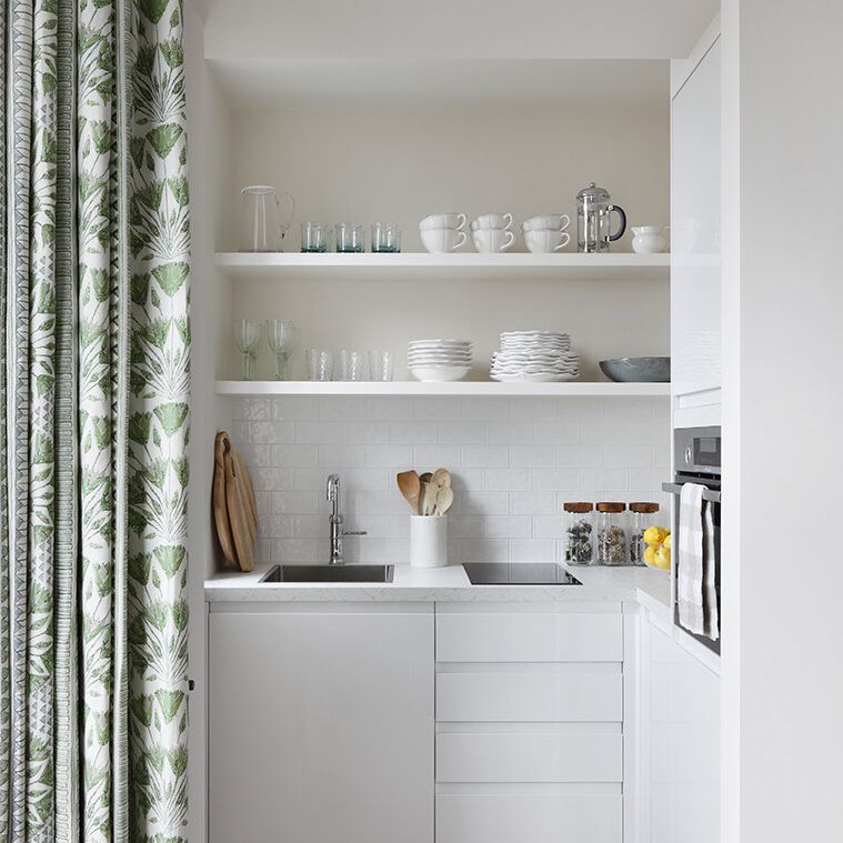 一个小型的白色厨房，用绿色印花窗帘分开