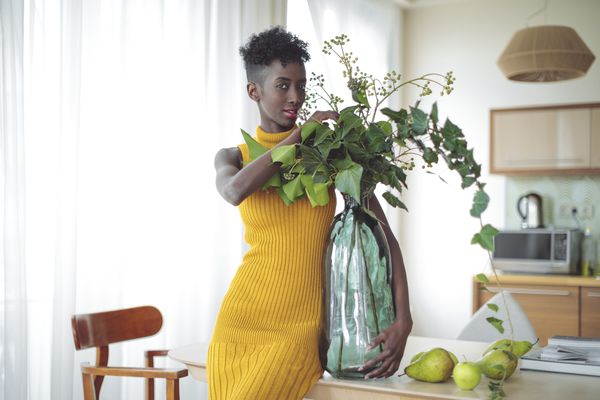 一位年轻的黑人妇女，穿着黄色的衣服，手里拿着一个大花瓶，花瓶里有一株植物。