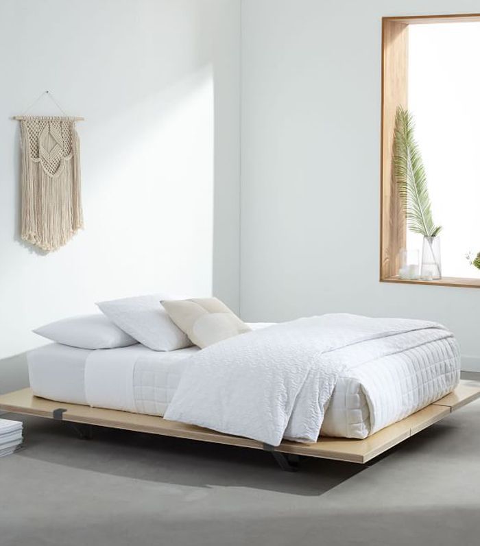 白色房间里的一张平台式床，上面铺着白色的床上用品，墙上挂着一面墙。