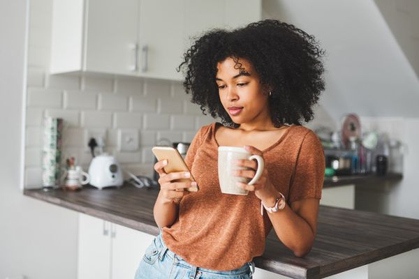 她的电话和饮用的咖啡的少妇在厨房里