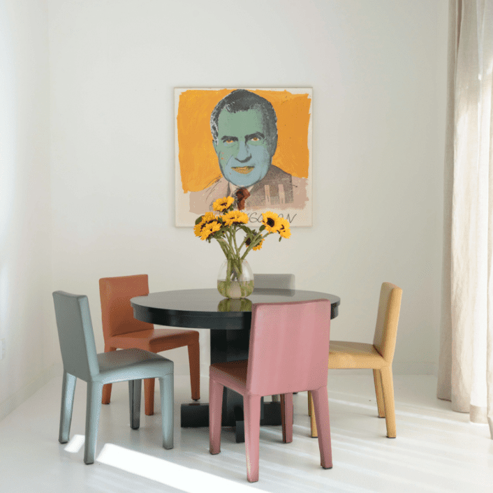 一张被彩色椅子环绕的桌子，旁边是一件现代艺术品