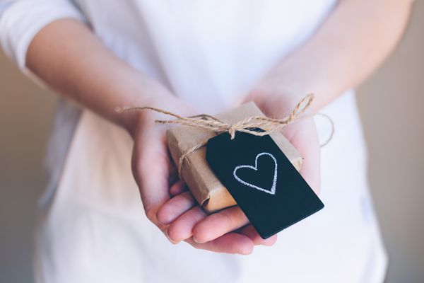 女孩的手握一个小礼物与粉笔心形黑色瓷砖