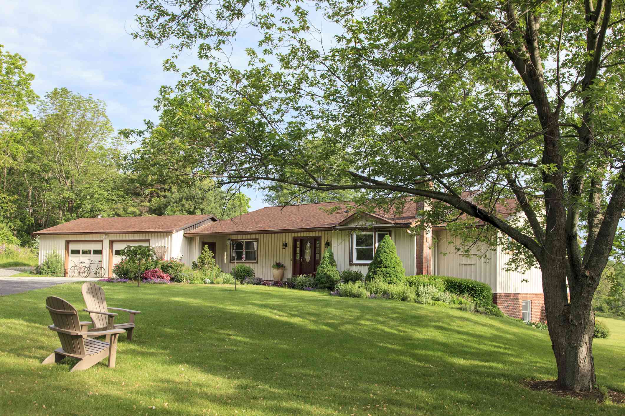 牧场风格的房子，带有郁郁葱葱的绿色草坪，有两把阿迪朗达克椅子和树