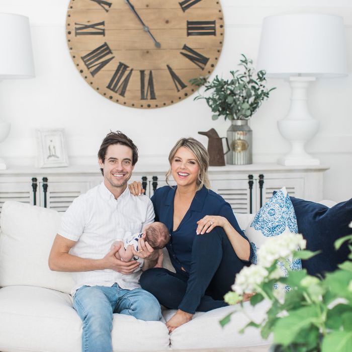 告别单身女郎阿里·费多托斯基回家之旅:阿里和丈夫凯文抱着他们刚出生的孩子，坐在白色的沙发上