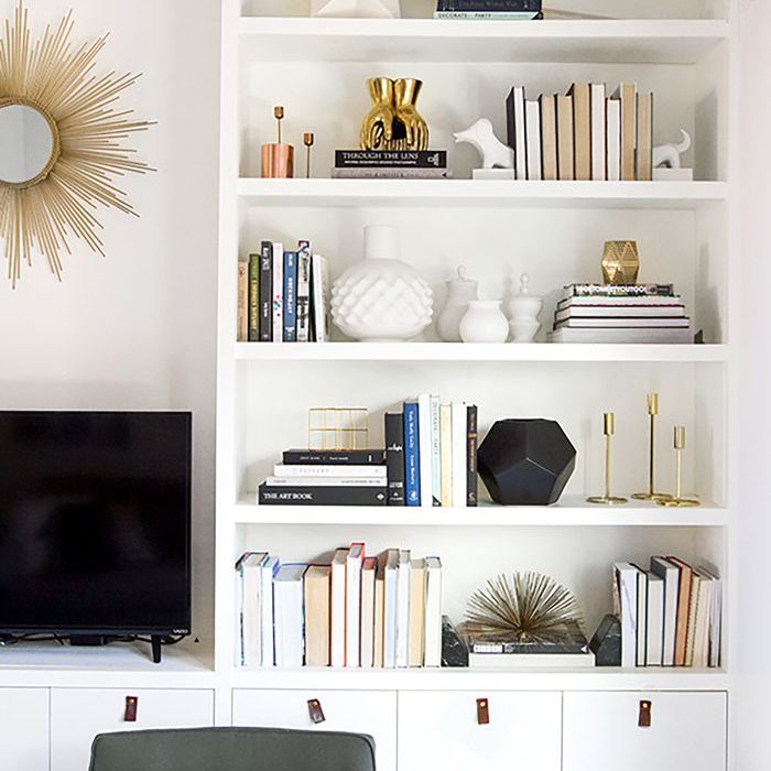 白色的客厅，嵌壁式的书架上摆放着书籍和白色的物品”class=