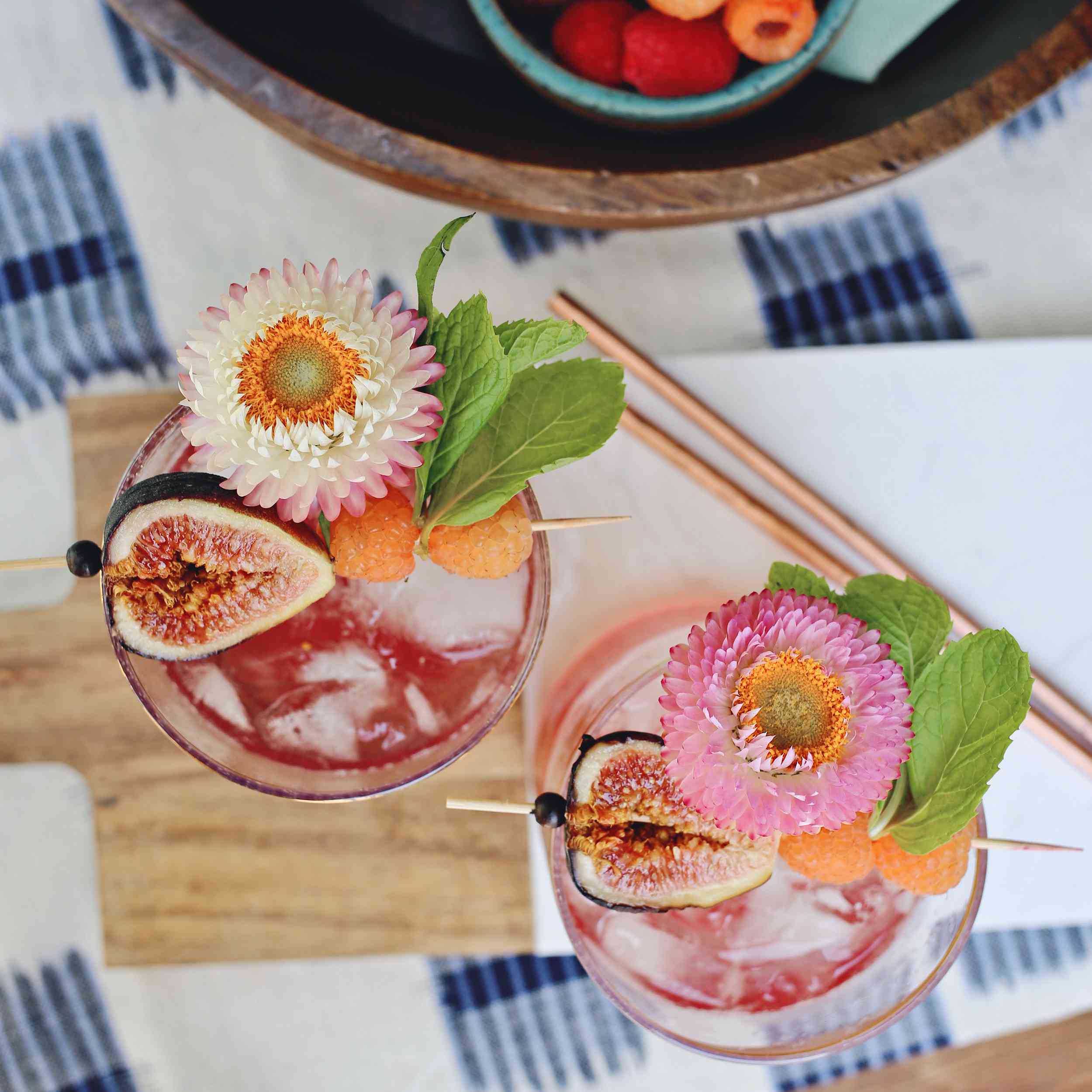 从头顶上看粉红色的鸡尾酒与无花果，覆盆子和花在木板和蓝白桌布上