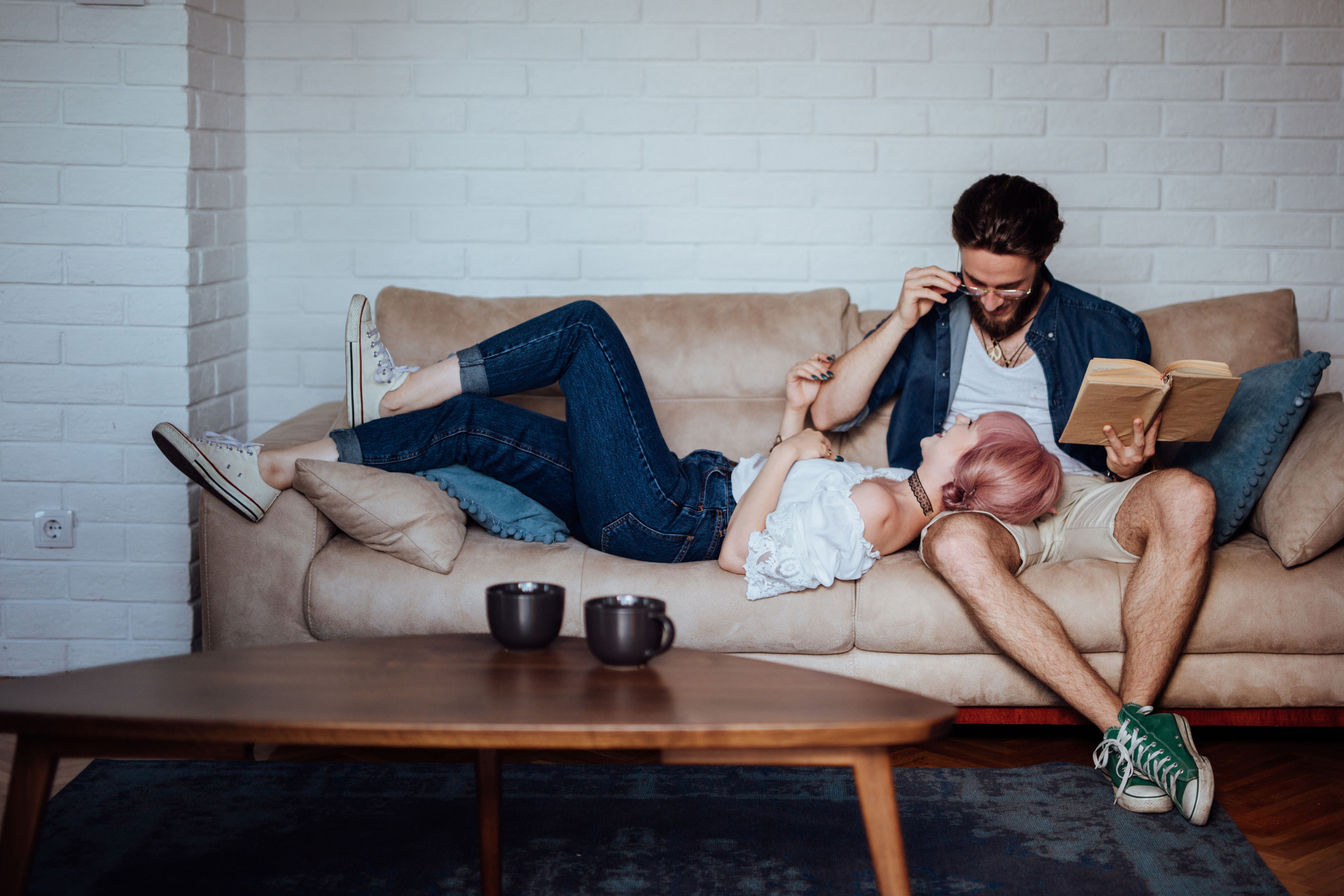 年轻的情侣在沙发上，一个与书在手，其他与她的头在他的大腿上