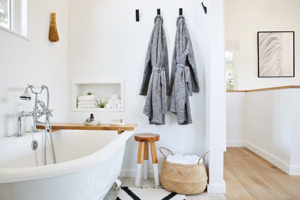 White clawfoot bathtub in a beautiful white rustic modern design farmhouse tiny house bathroom with linen bathrobes, stool, towels and essential oil